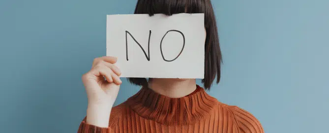 Woman covers her face with a sign that says 'NO'